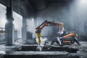 En orange Husqvarna rivningsrobot arbetar i en dammig inomhusmiljö.